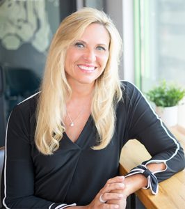 Image of President and CEO Deb Rishel in black blouse with white sleeve details sitting at Paradigm Digital Group offices