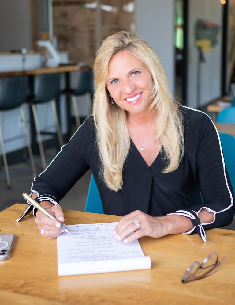 Image of President and CEO Deb Rishel in black blouse with white sleeve details writing notes on legal pad at Paradigm Digital Group offices