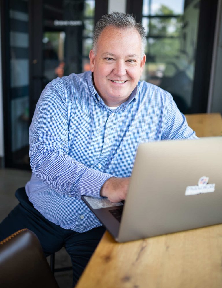Image of Vice President of Marketing Mike Curts in blue patterned button down with hands on laptop at Paradigm Digital Group offices
