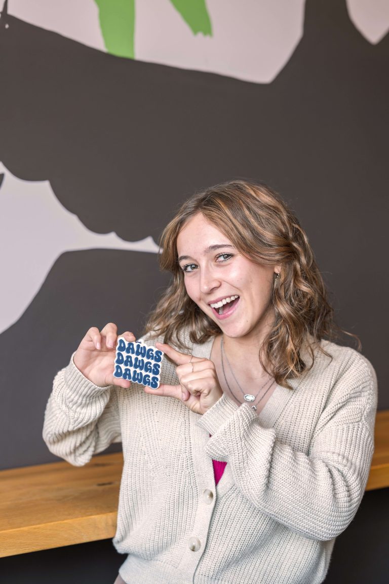 Image of Digital Content Intern, Rachel Sabotta, holding a "dawgs dawgs dawgs" plague representing Butler University, at Paradigm Digital Group offices