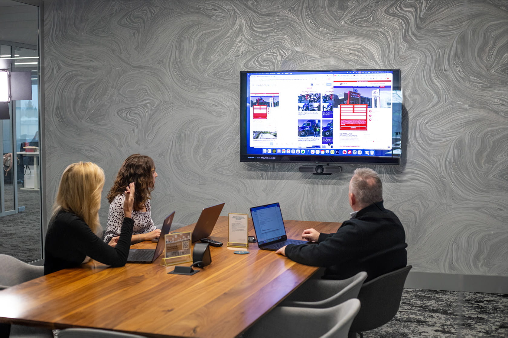 Deb, Rachel, and Mike sitting in conference room and looking at TV screen displaying a client website