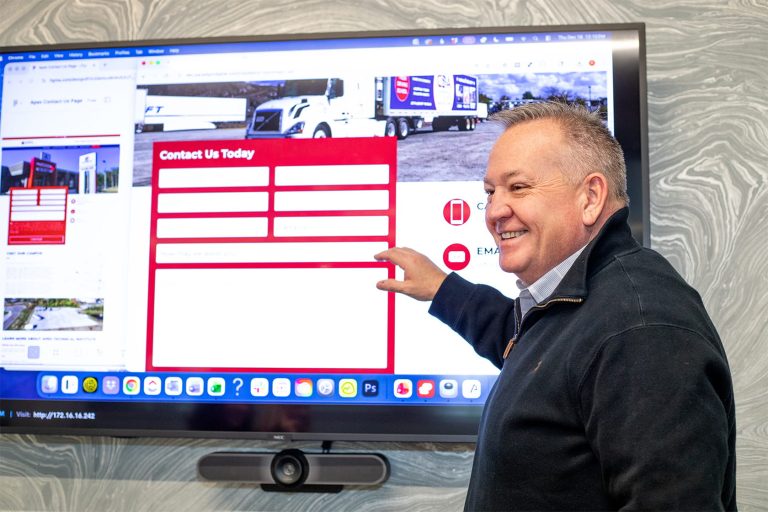 Mike smiling and gesturing toward TV displaying client website